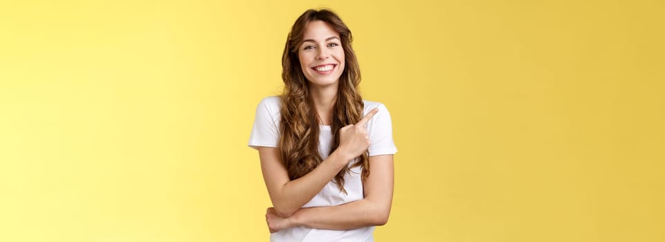 Cheerful charismatic good-looking gentle girl laughing silly amused entertaining conversation pointing upper left corner inviting check out try delicious coffee smiling broadly yellow background.