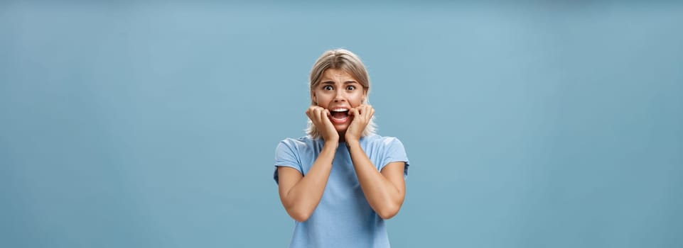 Lifestyle. Indoor shot of shocked troubled girlfriend hearing mom returned home being with boyfriend biting fingernails being in helpless perplexed situation feeling anxious and scared over blue background.