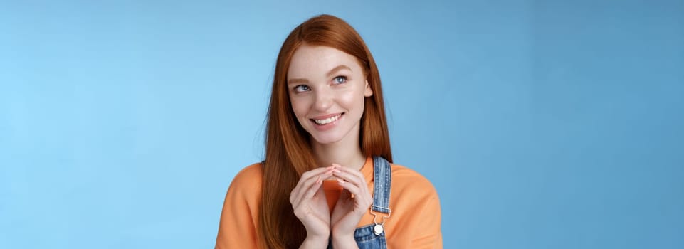 Devious tricky smart pretty redhead girlfriend have evil plan smirking mysteriously look upper left corner twiddles fingers think excellent plan, smiling delighted, standing blue background.