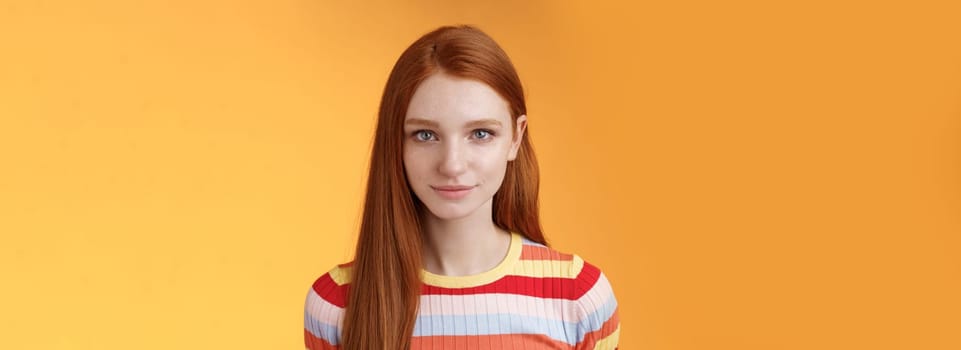 Attractive young sincere redhead girl clean pure perfect skintone smiling modest look camera friendly delighted standing relaxed awaiting gazing silly tenderly, posing orange background. Copy space