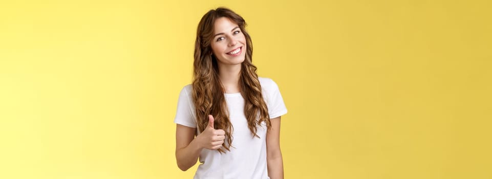 Well done congratulations. Happy charismatic pretty european female tilt head smiling broadly accept agree your idea like satisfied good result show thumb up approval gesture yellow background.