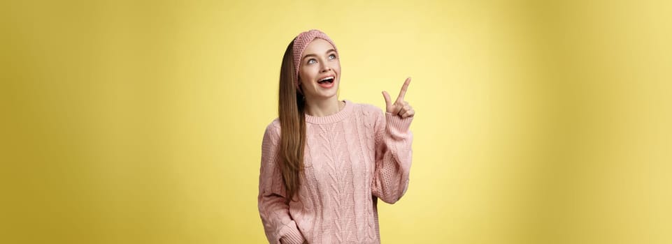 Amused and impressed dreamy pretty young european woman in knitted sweater gasping entertained dropping jaw smiling thrilled, joyful, pointing, looking at upper left corner excited of awesome promo.