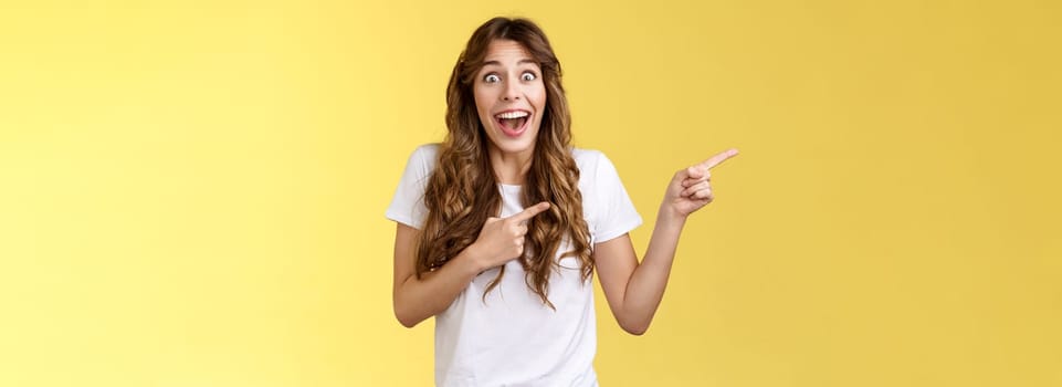 Happy sincere cheerful young surprised woman see celebrity lose speech stare excited unbelievable awesome luck fascinated pointing index fingers left open mouth stunned thrilled yellow background. Lifestyle.