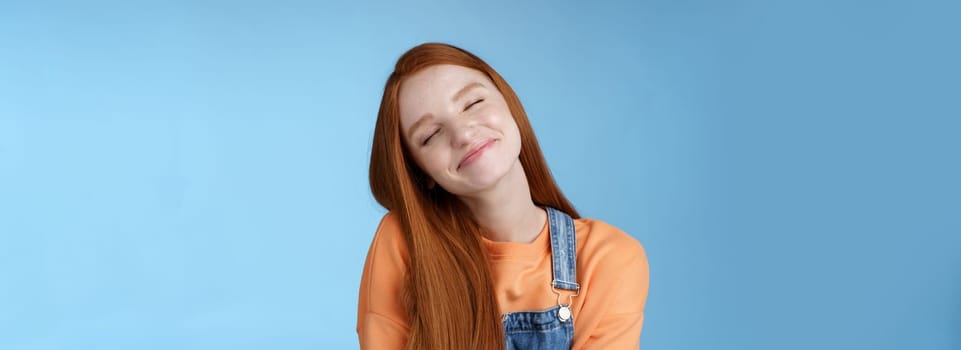 Dreamy kind silly redhead smiling happy girl straight long ginger hair daydreaming imagine romantic moment close eyes smiling delighted tilting head look joyful, standing blue background.