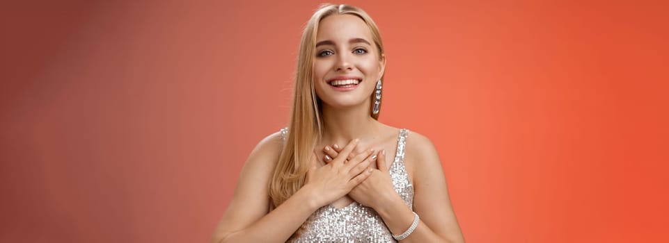 Grateful charming blond european 25s woman in silver party dress press palms heart feel thankful appreciate effort cherish romantic gesture receive flattering compliments gifts, smiling happily.