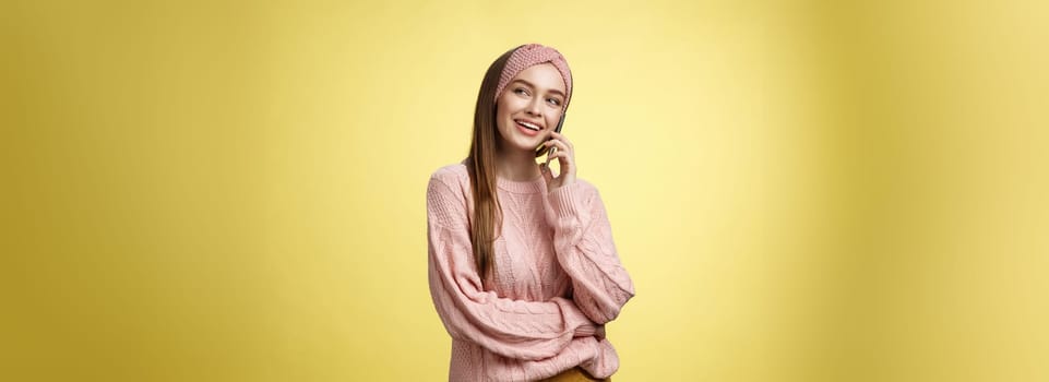 Talkative attractive glamour young 20s european woman wearing sweater, knitted headband tilting head looking away smiling curious, enjoying pleasant conversation via smartphone, talking to friend.