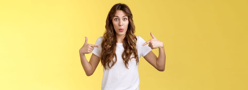 Wow just look. Impressed surprised cute wondered european girl pointing fingers center copy space white t-shirt folding lips amused astonished awesome promo great chance gaze you camera.