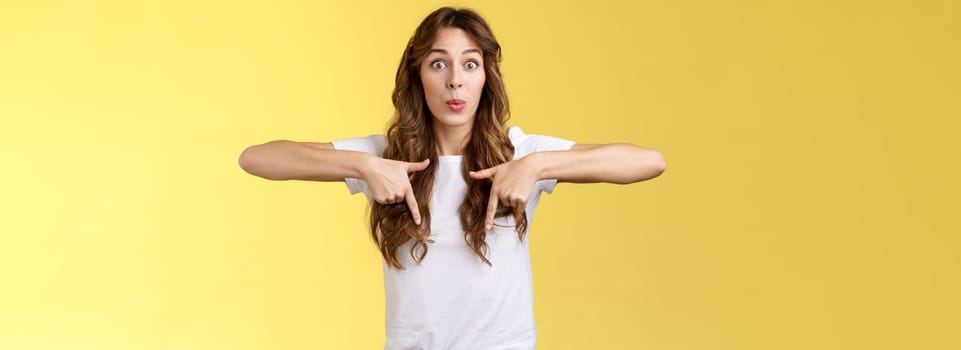 Fascinated impressed charismatic brunette female curly long haircut folding lips whistle astonished react excited thrilled telling you incredible promotion pointing down bottom yellow background.