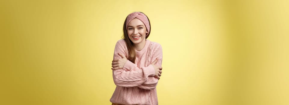 Getting chilly, better put on coat. Charming cute young tender european woman wearing sweater embracing body cross arms over chest, hugging herself to warm-up feeling cold, trembling, smiling.