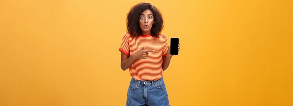 Portrait of impressed and curious female friend showing profile of ex to friend talking about shocking changes of appearance folding lips from interest holding smartphone pointing at cellphone screen. Lifestyle.