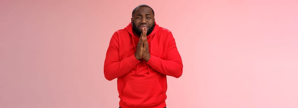 Miserable african american man beard in red hoodie stooping make supplicating upset grimace grying sobbing asking help say please hold hands pray begging mercy, apologizing need money.