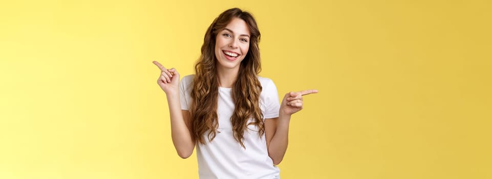 Girl have two suggestions pointing sideways. Cheerful charismatic curly-haired attractive woman pointing left right index fingers introduce promo products smiling broadly lively recommend ad.