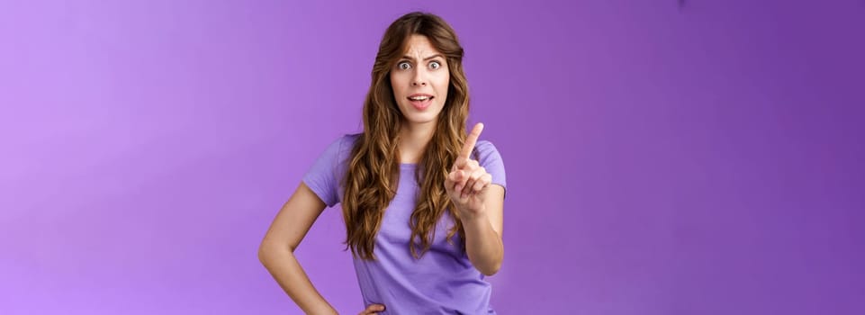 Displeased offended serious-looking assertive woman forbid express dislike and disapproval frowning annoyed shaking index finger prohibit refusing offensive behaviour stand purple background.
