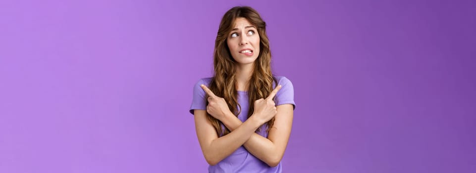 Hesitant unsure worried girl complicated make difficuly choice frowning nervously deciding look away pointing sideways cross hands chest left right anxiously choosing doubtful purple background.