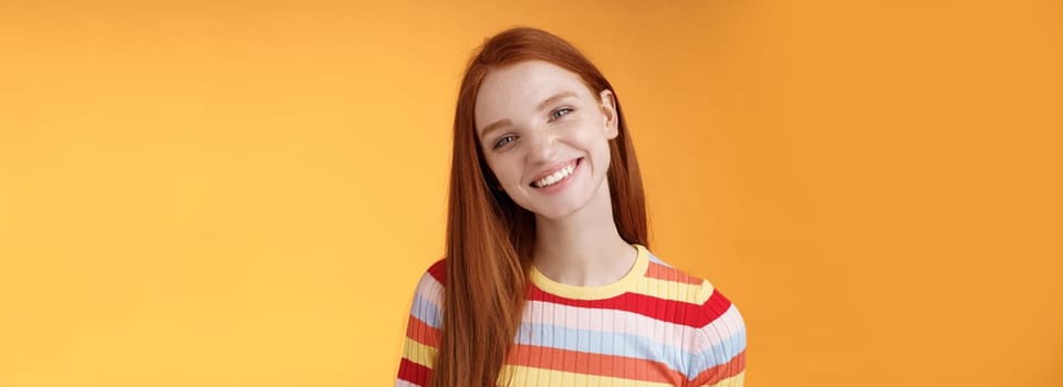 Pleasant charismatic young confident carefree redhead charming girl tilting head smiling broadly white teeth talking casually good mood express positive happy emotions standing orange background.