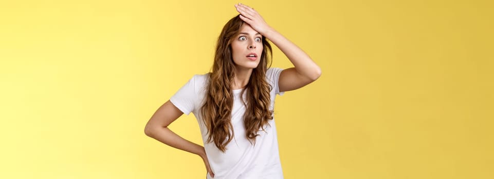 Oh gosh how stupid. Shocked embarrassed ambushed curly-haired girl popping eyes punch forehead make facepalm gasping stare aside bothered forgot cancel appointment stand yellow background.