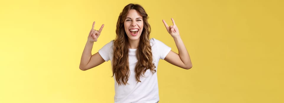 Girl having fun excellent awesome concert enjoy live music show rock-n-roll heavy metal gesture yelling upbeat happy attend cool festival party smiling broadly show tongue daring yellow background. Lifestyle.