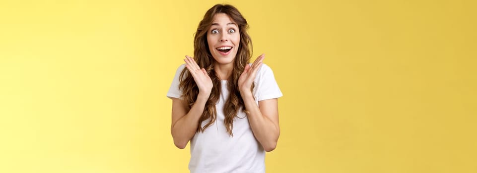 Surprised happy pleased impressed curly-haired girl gaze camera admiration satisfaction joy clap hands cheerful smiling broadly look camera fascinated enthusiastic applause yellow background.