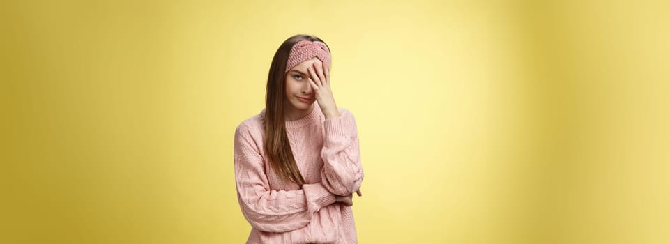 Woman facepalming covering face annoyed, bothered and inrritated, smirking looking with dismay, pissed off, posing unhappy displeased, staring indignant and upset posing tired over yellow background.