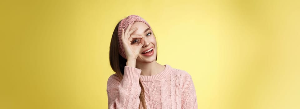 Let me see closer. Cute glamour young stylish european woman wearing knitted sweater, headband tilting head joyfully smiling intrigued positive showing circle over eye peeking at camera playful.