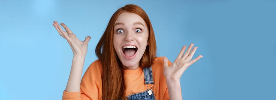 Surprised astonished sensitive overwhelmed young happy redhead girl receive incredible fantastic prize wide eyes astonished raising hands triumphing win lottery celebrating joyfully.