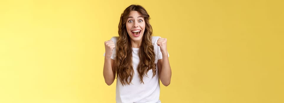 Cheerful supportive happy female fun fist pump relieved triumphing cheering rooting for favorite team winning smiling broadly hopefully look camera celebrating victory yellow background.