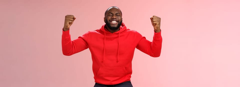 Happy thankful young african american bearded man thank god for son close eyes joyfully smiling clench fists celebrating triumphing dream come true accomplish goal, cheering victory.