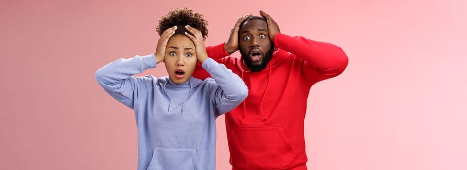 Shocked worried african american couple man woman holding hands head panicking widen eyes stunned receive bad concerning news feel troubled nervous, standing pink background anxious.