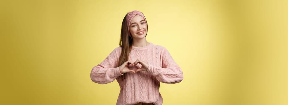 Girl brings peace and love, smiling tender, lovely showing heart gesture over chest, adoring, liking making romantic gestures feeling sympathy, passion and romance in air, posing in sweater.