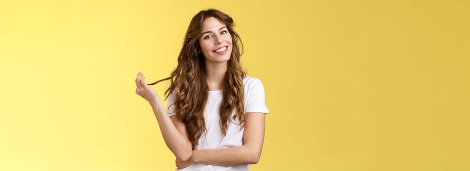 Silly cute feminine sensual curly-haired woman tilt head playing hair strand rolling curl smiling delighted interested listening flirty conversation coquettish gazing camera stand yellow background. Lifestyle.