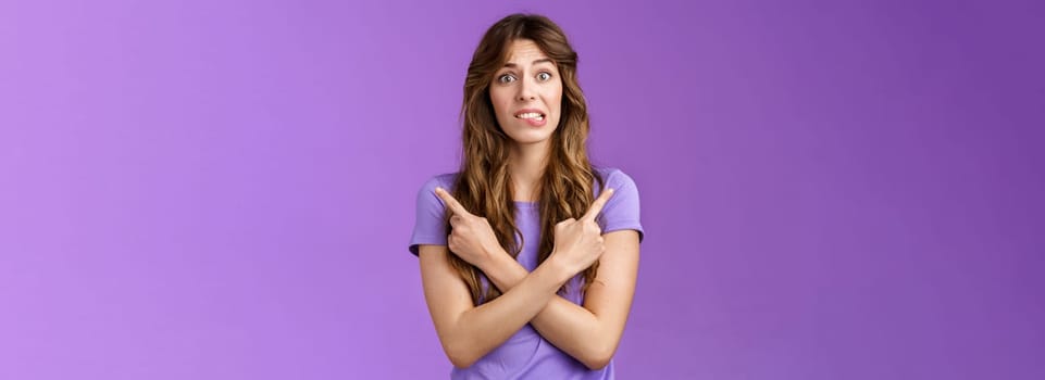 Perplexed timid hesitant worried girlfriend afraid making bad choice cross hands pointing sideways indicating left right perplexed decide frowning pull hesitant face asking advice purple background. Lifestyle.