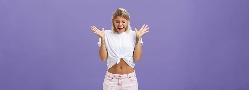 Studio shot of woman having mental breakdown screaming out loud shaking raised palms closing eyes and bending head down feeling scared and yelling from fear over purple background. Emotions concept