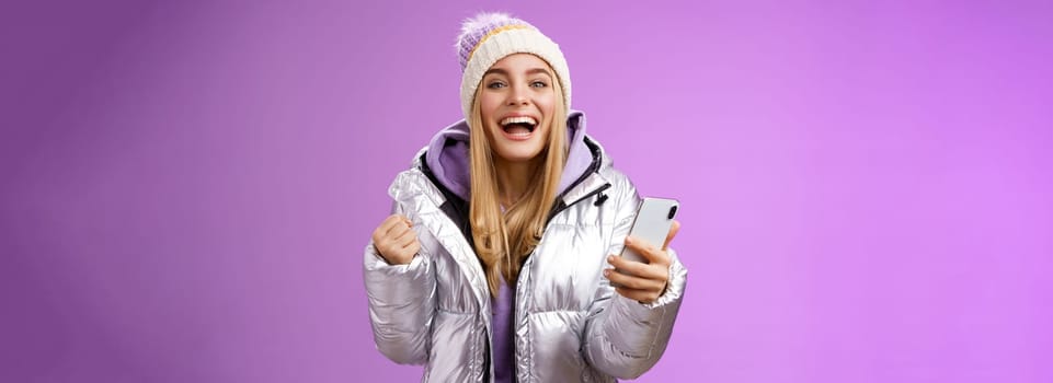 Happy lucky charming blond triumphing girl winning lottery first prize receive good news message smartphone clench fists celebrating success yelling yes accomplished, standing purple background.