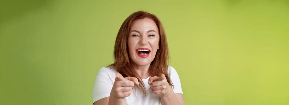 You did best. Friendly joyful enthusiastic redhead ginger middle-aged female pointing index fingers camera finger pistol gesture smiling broadly congratulate cheer coworker stand green background.