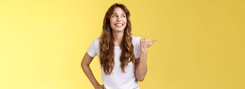 Satisfied carefree cheerful attractive european woman show thumb up pointing left turn aside pleased delighted expression discuss recent awesome purchase showing friend new car yellow background. Lifestyle.