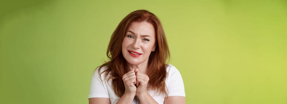 Silly touched tender redhead charmed middle-aged woman sighing gladly gaze admiration delighted press hands together heartwarmed fascinated look grateful lovely camera green background.