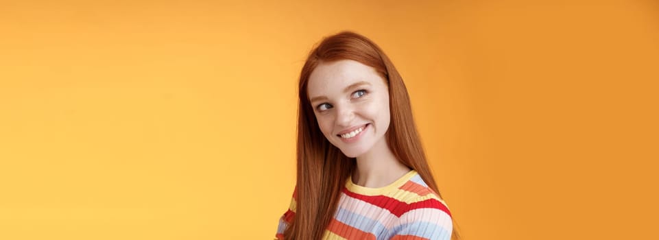 Silly flirty good-looking redhead girl making first move checking out guy standing profile turning left smiling intrigued glancing aside coquettish flirting seducing sassy, orange background.
