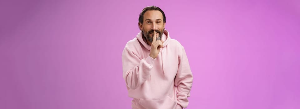 Lips sealed secret. Portrait alluring cheeky stylish adult bearded guy in pink hoodie asking keep quiet show shush shh gesture index finger pressed mouth smiling devious smug face, have idea.