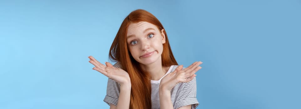 Lifestyle. Unsure clueless cute silly redhead female part-time worker shrugging careless raise hands unaware smirking tilting head lift eyebrows confused cannot answer no idea standing blue background.