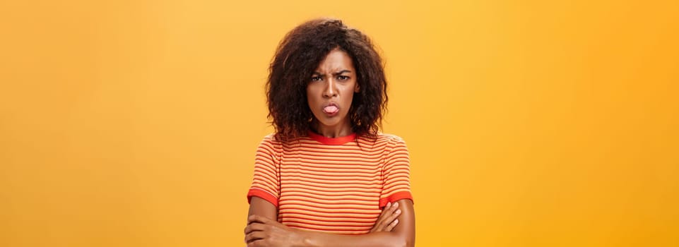 You offended me apologize. Displeased childish attractive adult woman in striped t-shirt holding hands crossed sticking out tongue and frowning having bad temper being dissatisfied and angry.