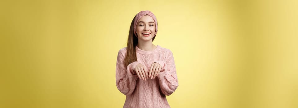 Girl pretends easter bunny. Charming cute female in knitted sweater holding palms like rabbit smiling happily, mimicking pretty animal fooling around from happiness and joy against yellow background.