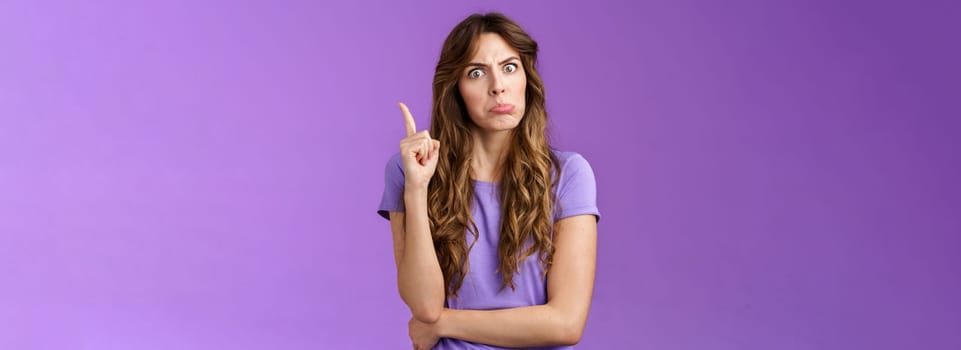 Strict funny curly-haired girl pulling disappointed angry face popping eyes stare camera shaking index finger disapproval scold bad behaviour stand serious bossy purple background.