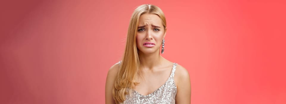 Disappointed complaining cute blond woman in silver stylish dress grimacing frowning upset have bad day pouting pity standing displeased unhappy heartbroken everything bad, red background.