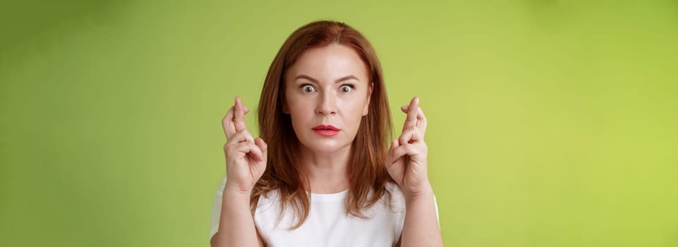 Stunned intense worried middle-aged redhead woman. stare nervously awaiting important result implore dream come true receive positive reply standing stupor green background make wish good luck.