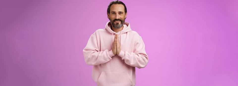 Peaceful attractive bearded mature mail model in trendy pink hoodie press palms together namaste praying gesture smiling delighted relaxed bowing buddhism faith, appreciating help, look thankful.