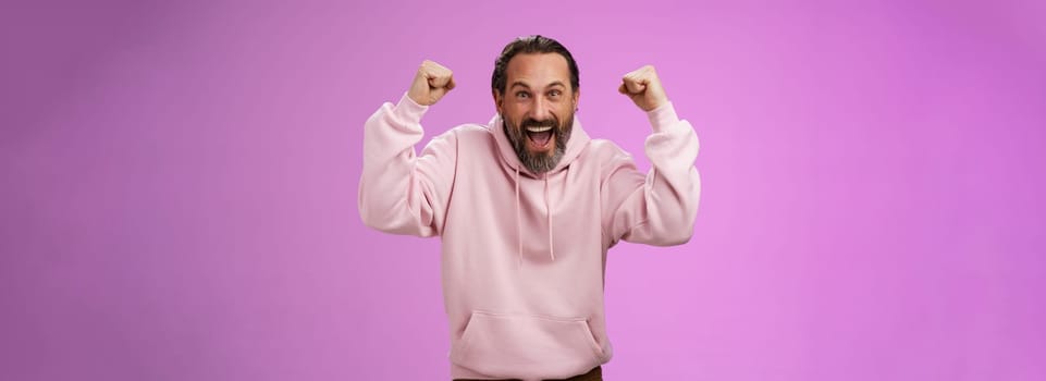 Excited cheering devoted male bearded grey hair yelling supportive words win lottery place good lucky bet standing pleased triumphing say yes raising fists victory success gesture, purple wall.