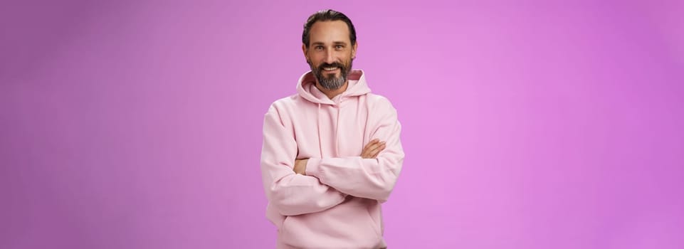 Portrait cool bearded mature grandad trying stay stylish urban trends wear pink hoodie cross arms chest casual pose smiling happily talking have conversation, posing purple background.