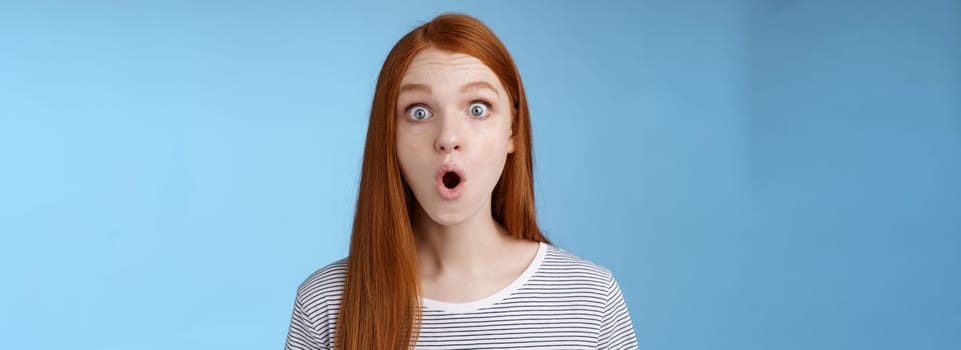 Wow omg fascinating. Impressed surprised amused good-looking redhead girl folding lips astonished wide eyes stunned reacting incredible cool promo standing blue background speechless.