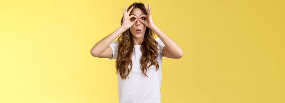 Wow so cool. Girl obersve interesting awesome event show okay perfection gesture look through ring hands folding lips amused wondered glance camera fascinated admiration interested yellow background.