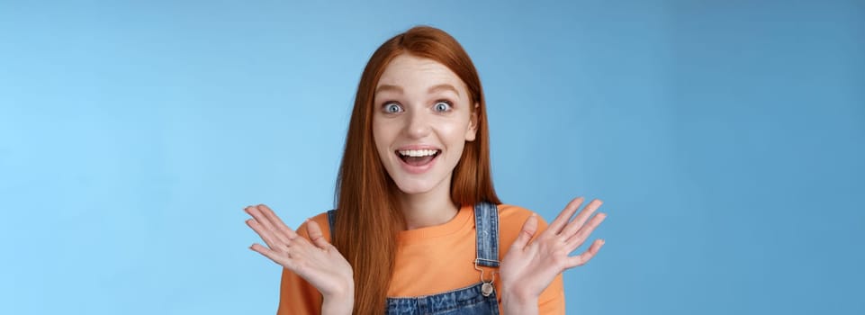 Surprised delighted happy friendly-looking amused redhead female friend learn incredible good news congratulating girlfriend fascinated wide eyes camera joyfully clap hands amazed, blue background.